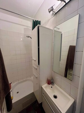 A bathroom with a bathtub, a sink, a mirror, and a towel rack. - Studio Jules Joffrin, dernier étage - Montmartre (Paris)