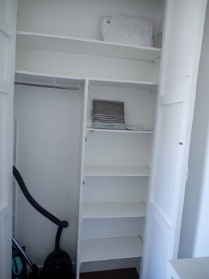 A white closet with multiple shelves, a hanging rod, and a suitcase. - Studio Jules Joffrin, dernier étage - Montmartre (Paris)