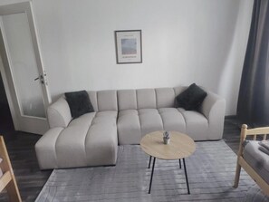 Ein modernes Wohnzimmer mit einem Ecksofa, einem runden Couchtisch und einem gerahmten Bild an der Wand.