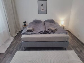 Ein Schlafzimmer mit einem Bett, zwei Nachttischen, einem Wandbild und einem Fenster mit Vorhängen.