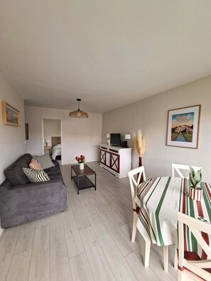 A living room with a sofa, a coffee table, a TV stand, and a dining area with chairs and a table. - Basque-style apartment in the heart of Cambo, near the thermal baths (Cambo-les-Bains)