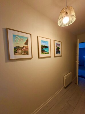 A hallway with three framed pictures on the wall, a hanging light fixture, and a radiator. - Basque-style apartment in the heart of Cambo, near the thermal baths (Cambo-les-Bains)