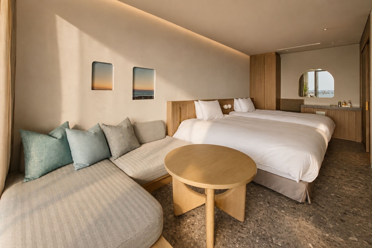 A hotel room with a large bed, a sofa, a small table, and a bathroom with a mirror.