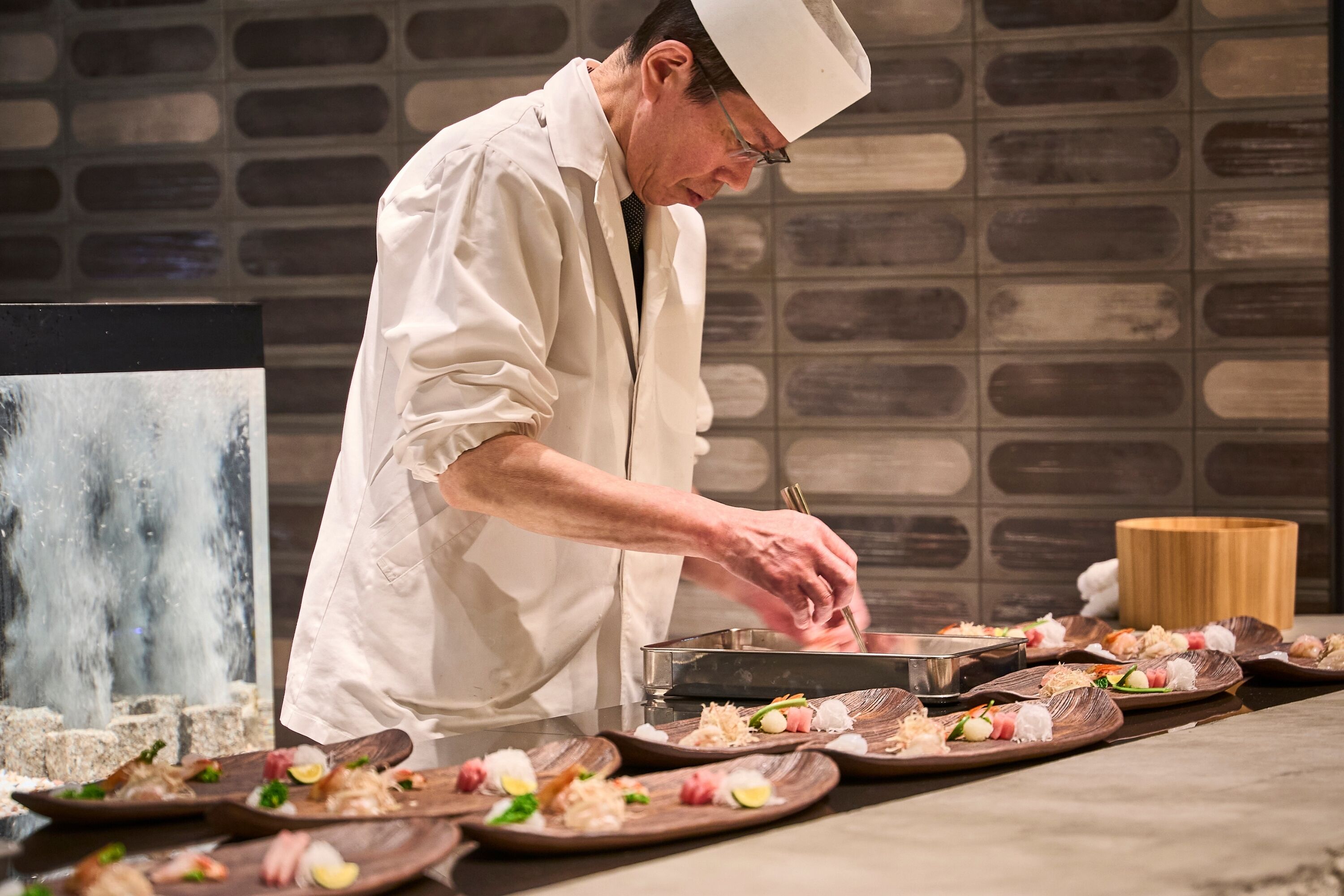 A chef in a white uniform preparing sushi at a counter with multiple plates of sushi.