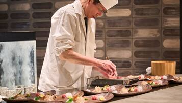 A chef in a white uniform preparing sushi at a counter with multiple plates of sushi.