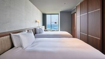 A hotel room with two beds, a large window with a view of the sea, and a wooden wardrobe.