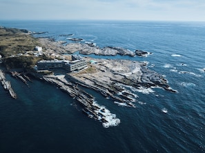 A coastal hotel with a rocky shoreline, a building with multiple floors, and a view of the ocean.