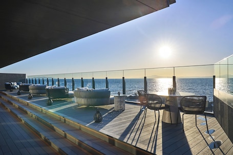 A sunlit deck with outdoor seating, a pool, and a view of the sea.