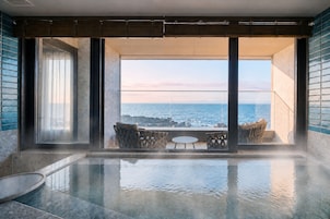 A spacious indoor area with a large window overlooking a body of water, a seating area with chairs, and a reflective floor.
