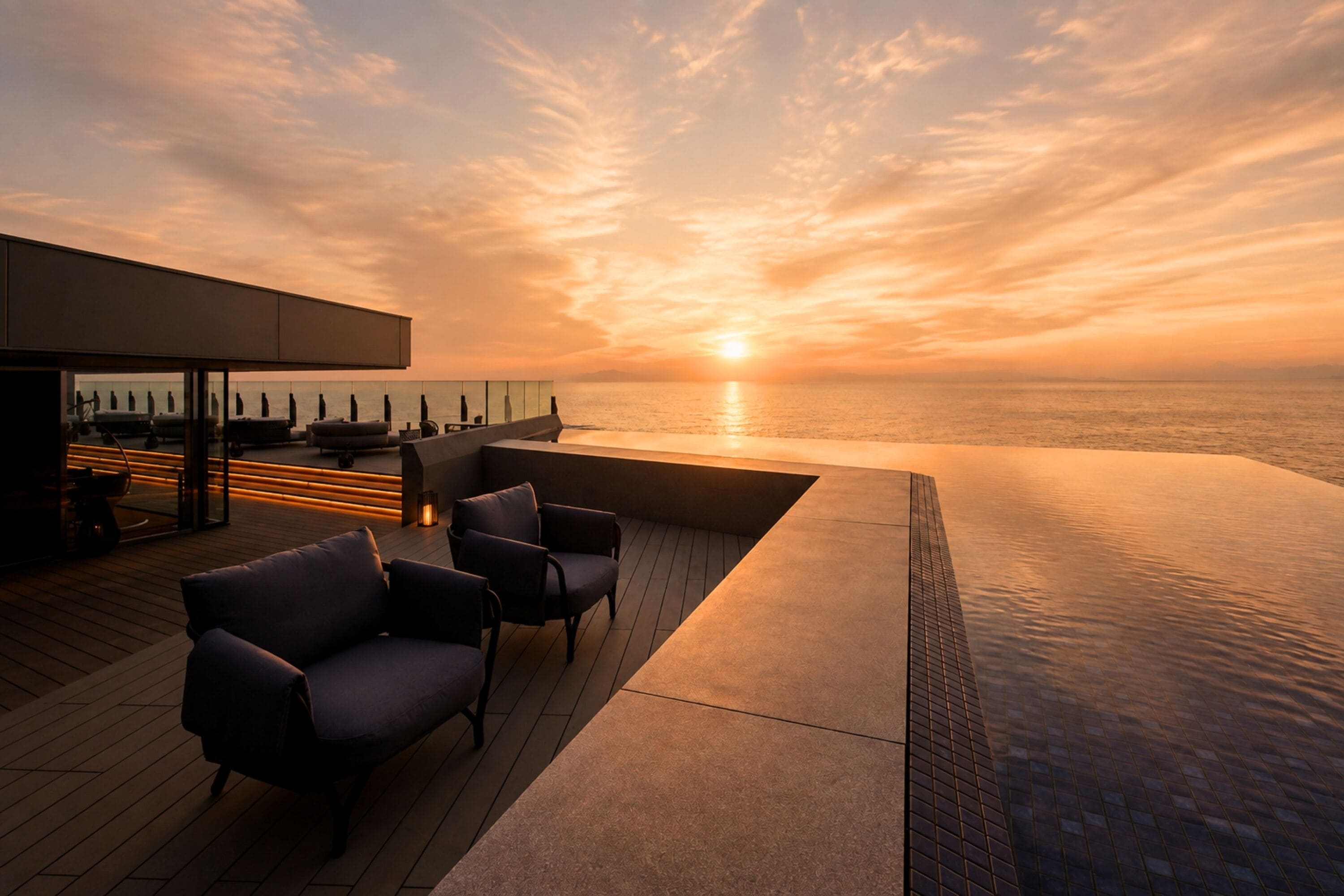 Eine Dachterrasse mit Blick auf den Sonnenuntergang über dem Meer, inklusive einer Sitzgelegenheit mit Stühlen und einem Tisch.
