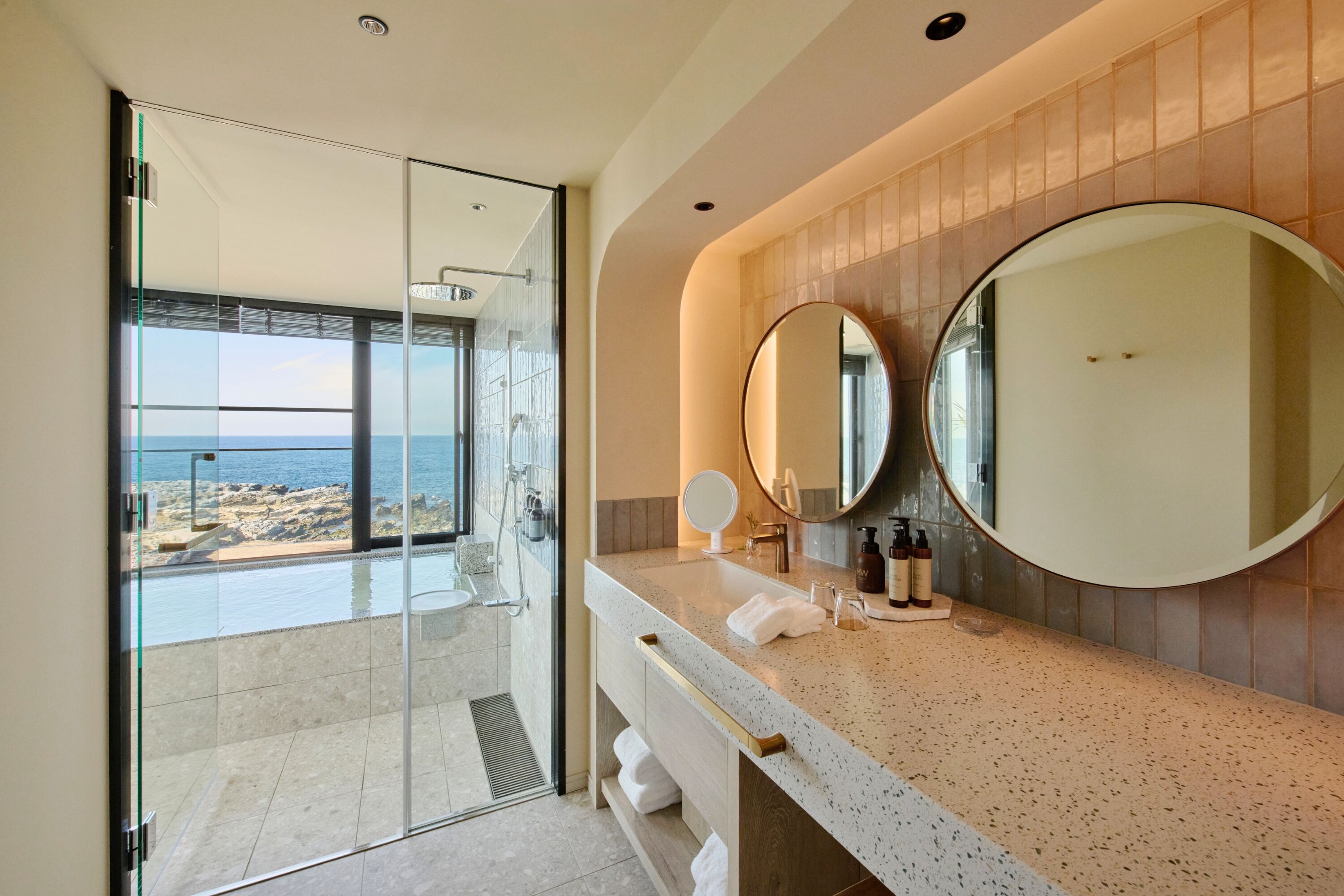 Une salle de bain moderne avec une douche à parois de verre, un grand miroir et une vue sur la plage.