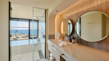 Une salle de bain moderne avec une douche à parois de verre, un grand miroir et une vue sur la plage.