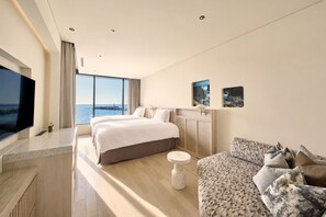 Habitación de hotel moderna con una cama grande, un sofá, un televisor y vistas al mar.