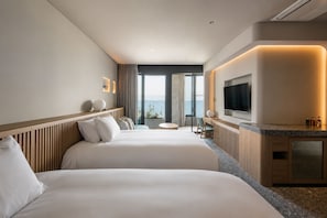 Quarto de hotel com duas camas, televisão e vista para o mar.