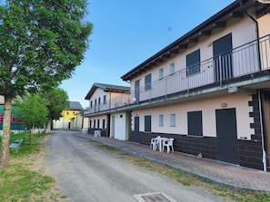 Una calle con edificios, un árbol y mobiliario exterior.