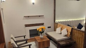 A modern room with a sofa, a small table with a vase, a fireplace, and a bed with a headboard. - Desert Oasis Camp And Resort (Leh)
