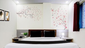 Una habitación de hotel moderna con una cama grande, una mesita de noche, una lámpara y arte en la pared que representa árboles y flores.