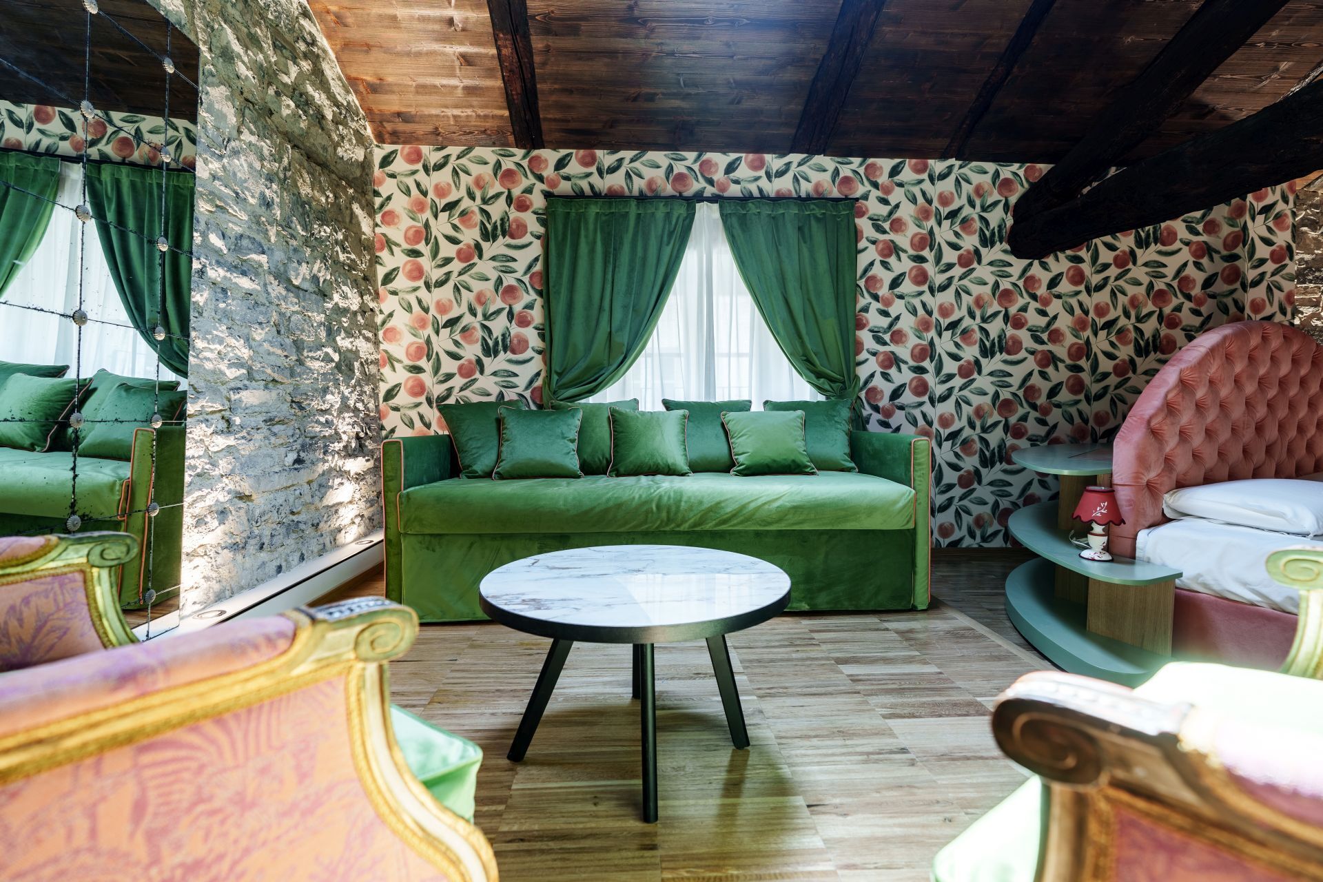 Une pièce avec un canapé vert, une table basse ronde et un fauteuil rose à motifs capitonnés.