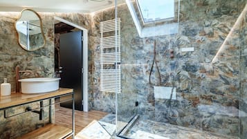 Un baño moderno con pared de piedra, cabina de ducha con vidrio y un espejo grande.