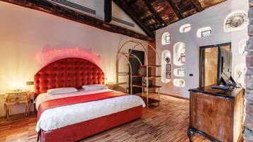 A bedroom with a red upholstered headboard, a wooden floor, a desk with a mirror, and a wall with circular cutouts.