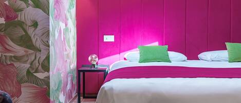 A modern hotel room with a vibrant pink accent wall, a bed with white and green pillows, and a neon sign.