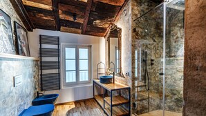 Une salle de bain avec un plancher en bois, une fenêtre, un lavabo avec un receveur bleu et un espace douche.