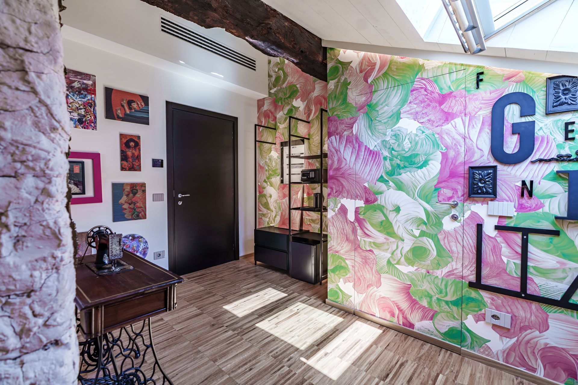 A room with a large floral mural, a black door, and a sewing machine on a wooden table.