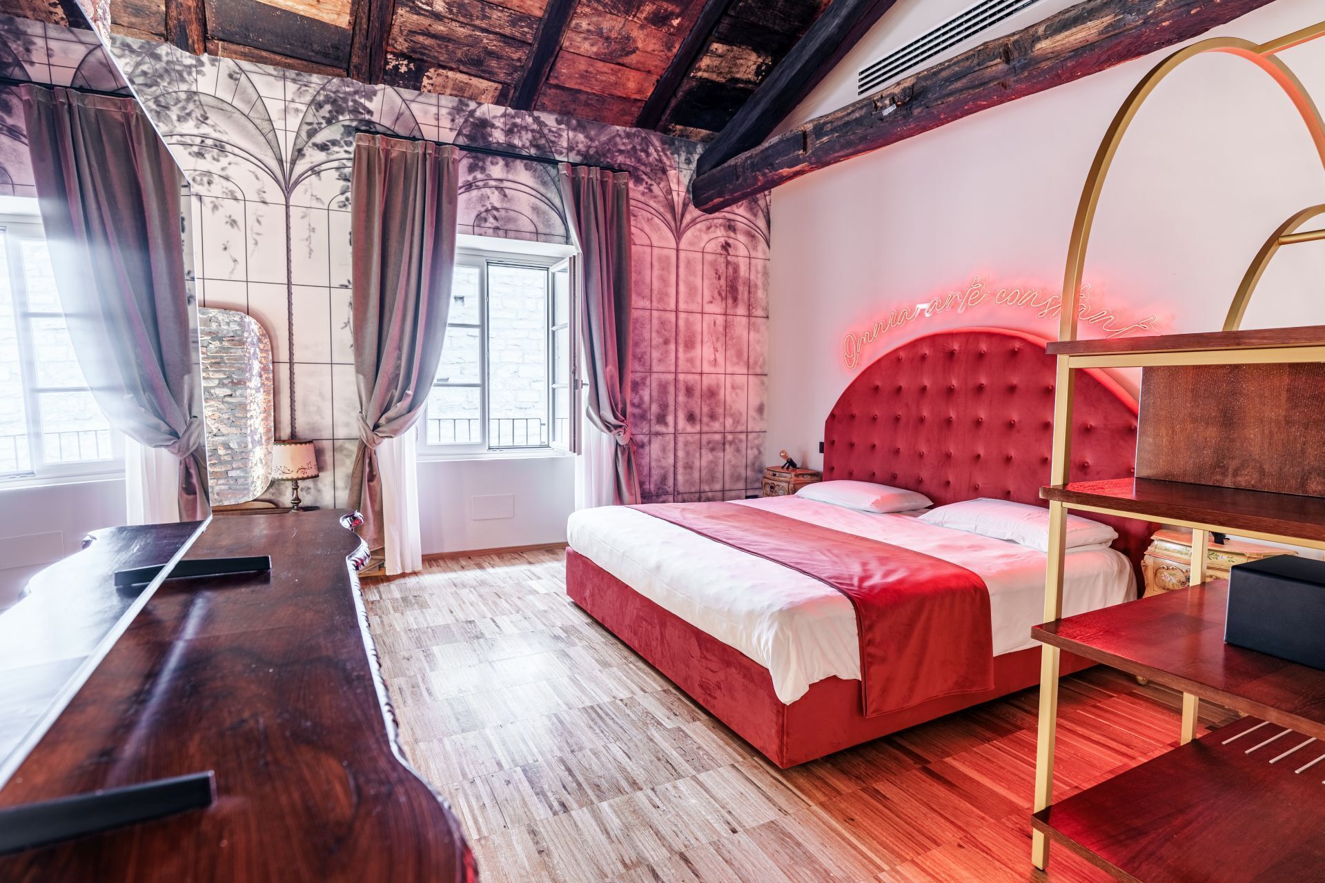 Une chambre avec un lit rouge, des meubles en bois, un mur en pierre et une fenêtre avec des rideaux.