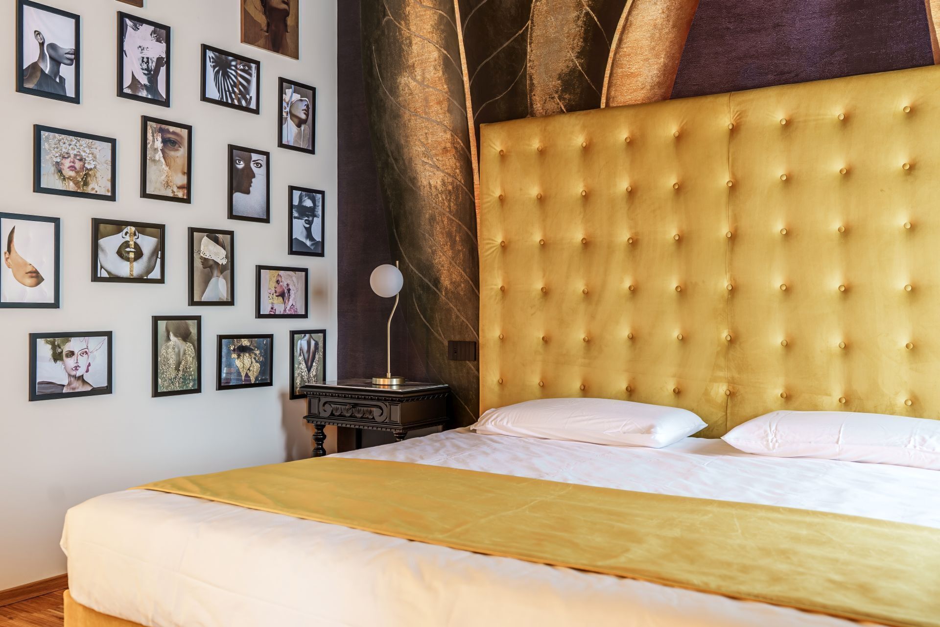 A bedroom with a large bed, a headboard, and a wall decorated with framed pictures.