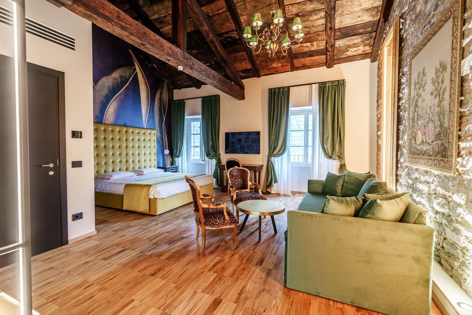 A room with a bed, a green sofa, a chair, a wooden ceiling, and a painting on the wall.