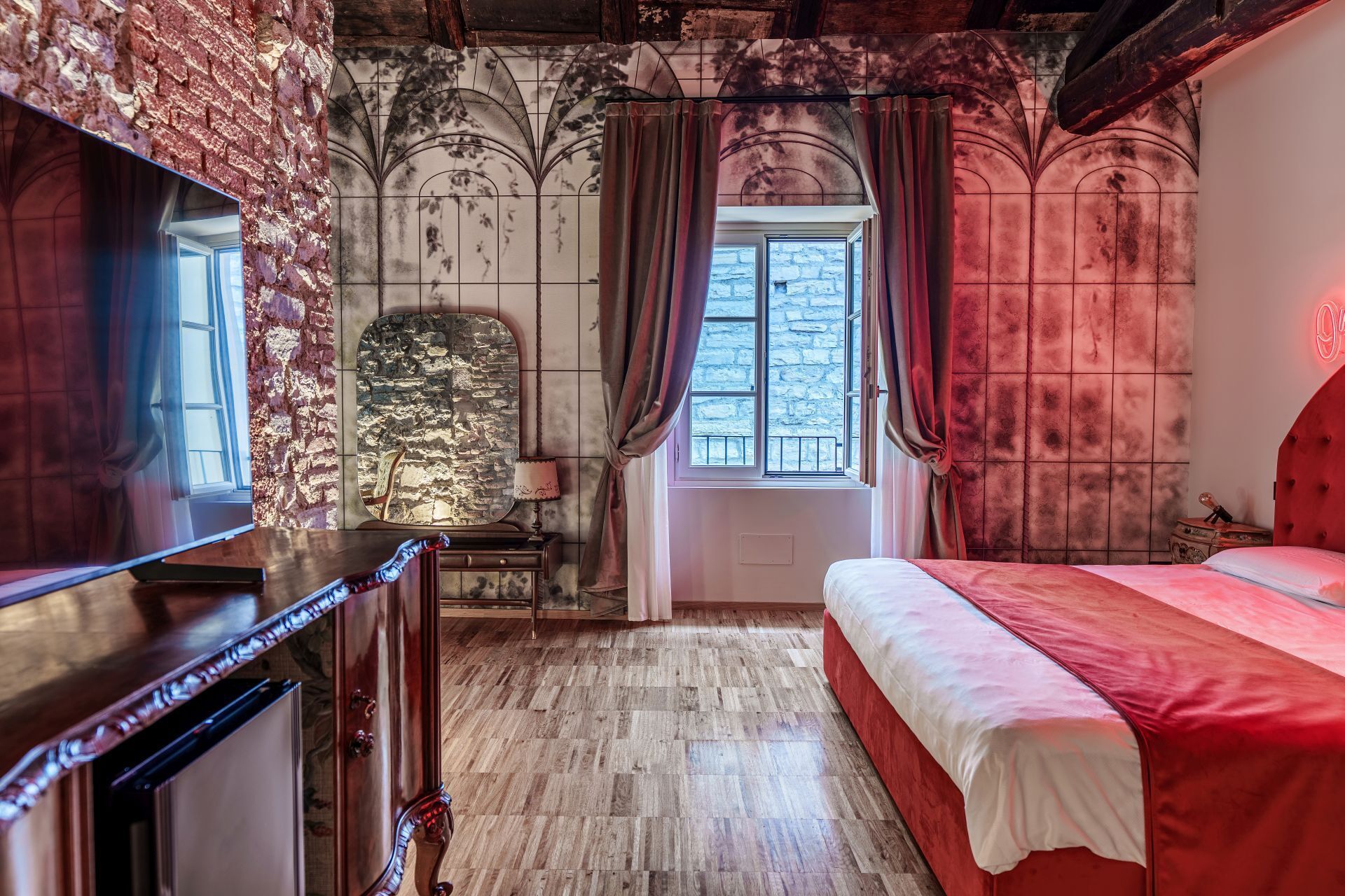Un dormitorio con cama, espejo, c ómoda, ventana y pared de piedra.