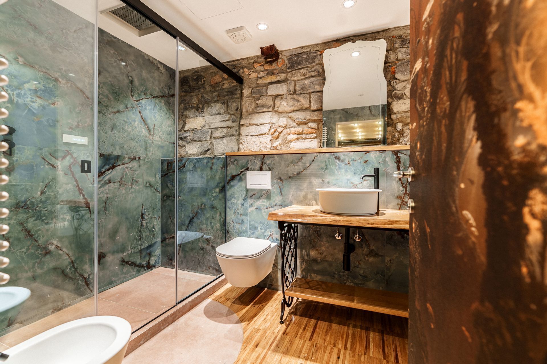 A modern bathroom with a glass shower enclosure, a freestanding bathtub, a sink with a wooden countertop, and a stone wall backdrop.