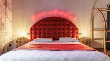 Habitación de hotel con una tapicería roja con textura en la cabecera, un letrero de neón sobre la cama y una mesita de noche de madera con una lámpara.