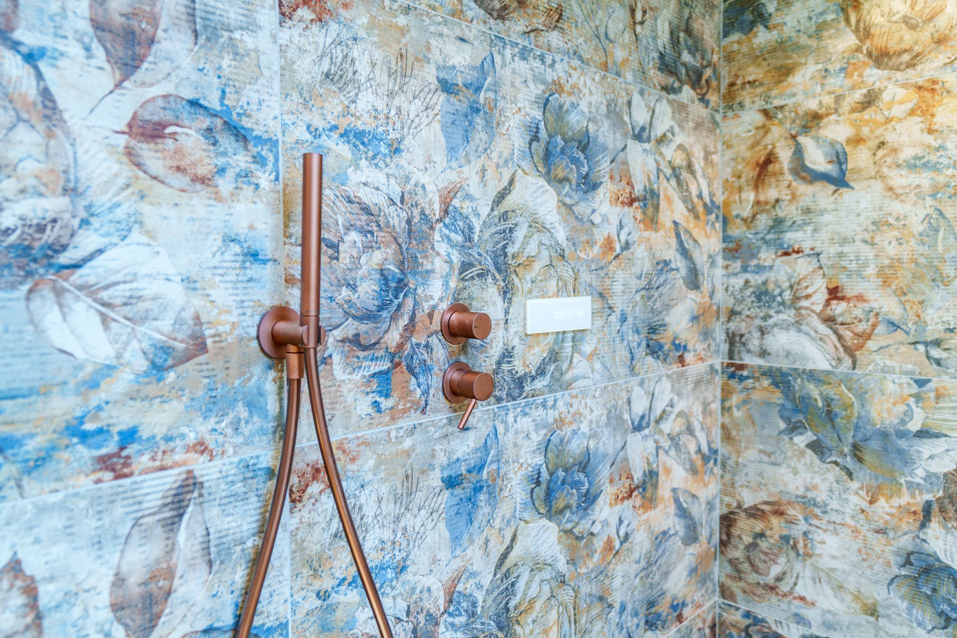 A bathroom with a floral tile wall, a shower with a single-handle faucet, and a small white label.