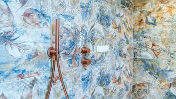 A bathroom with a floral tile wall, a shower with a single-handle faucet, and a small white label.