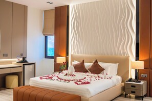 A hotel room with a bed, bedside tables, a desk, and a window.