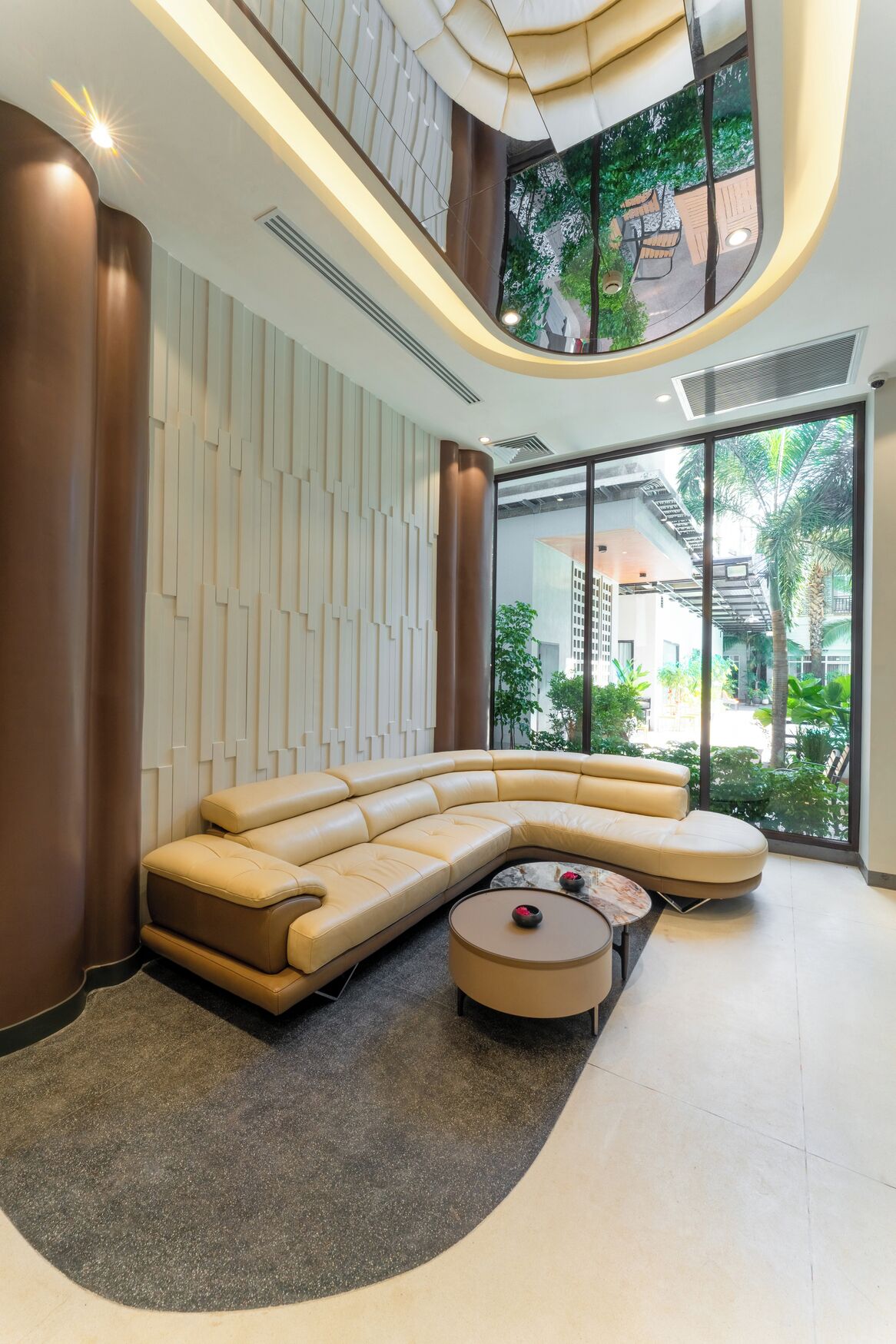 Un interior moderno con un sofá modular curvo, una mesa redonda y vistas a un área tropical exterior a través de grandes ventanales.