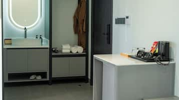 Een moderne badkamer met een wastafel, spiegel, badjas en een klein bureau met een koffiezetapparaat.
