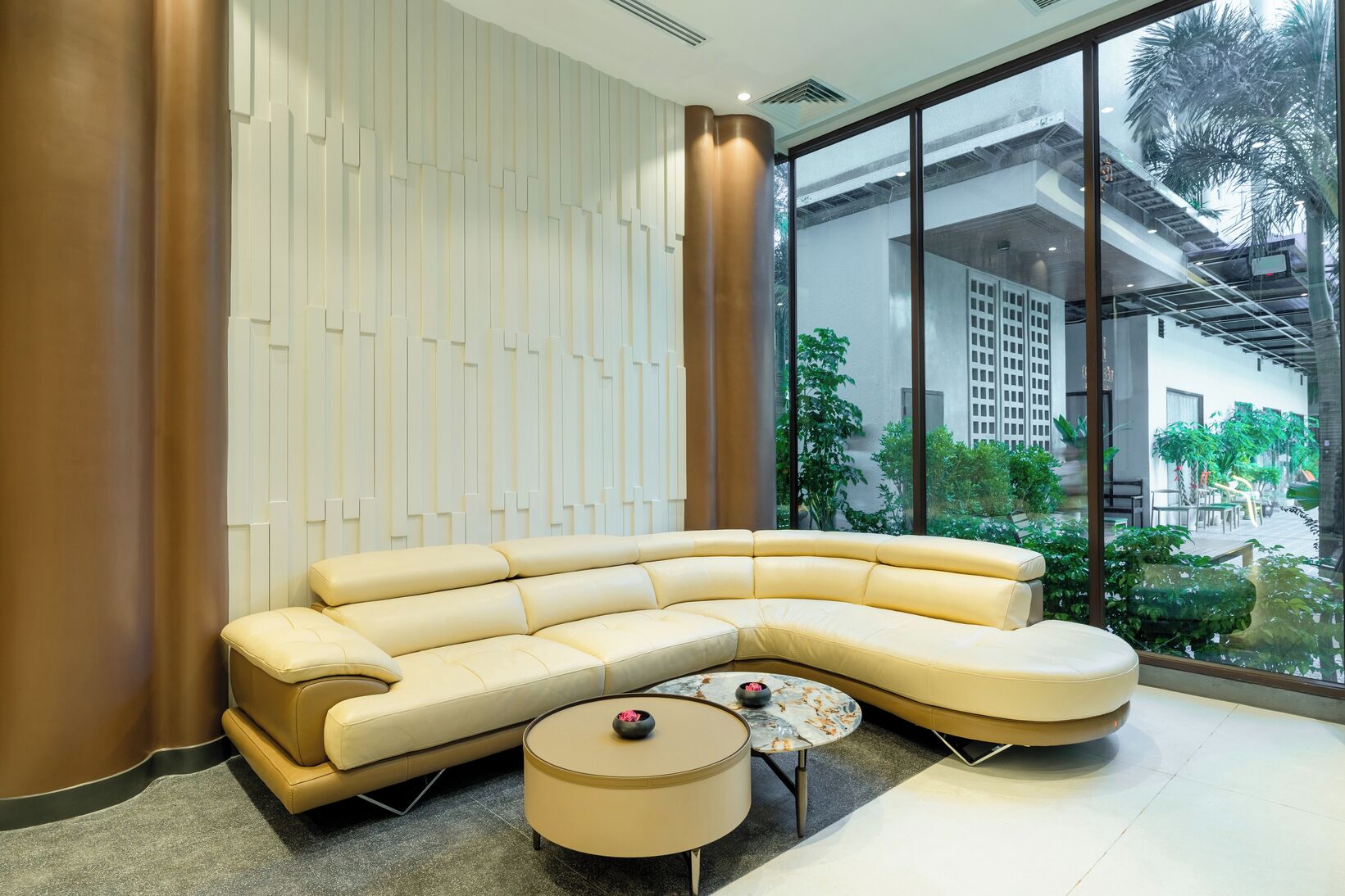 Ein modernes Wohnzimmer mit einer gebogenen Couch, einem runden Couchtisch und einem großen Fenster mit Blick ins Freie.