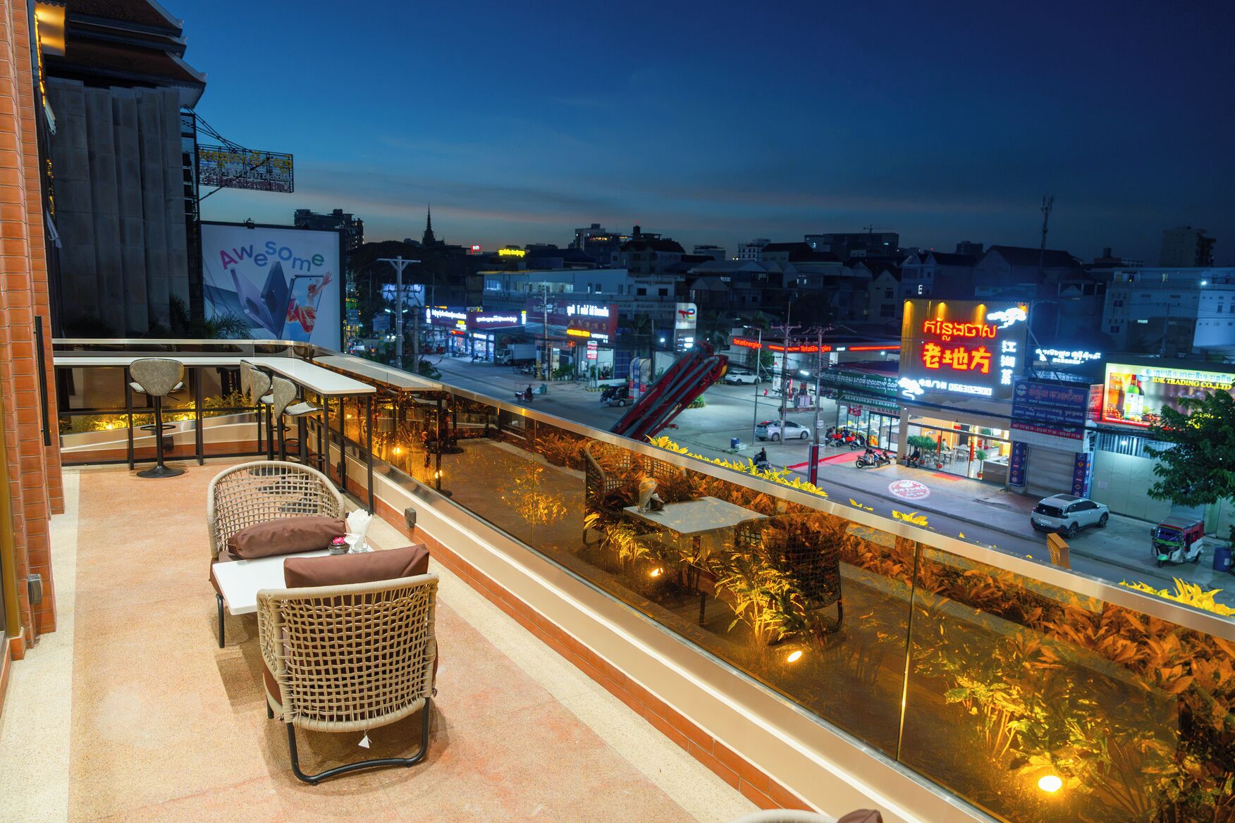 A balcony with wicker furniture, a view of a city street at dusk, and illuminated signs.