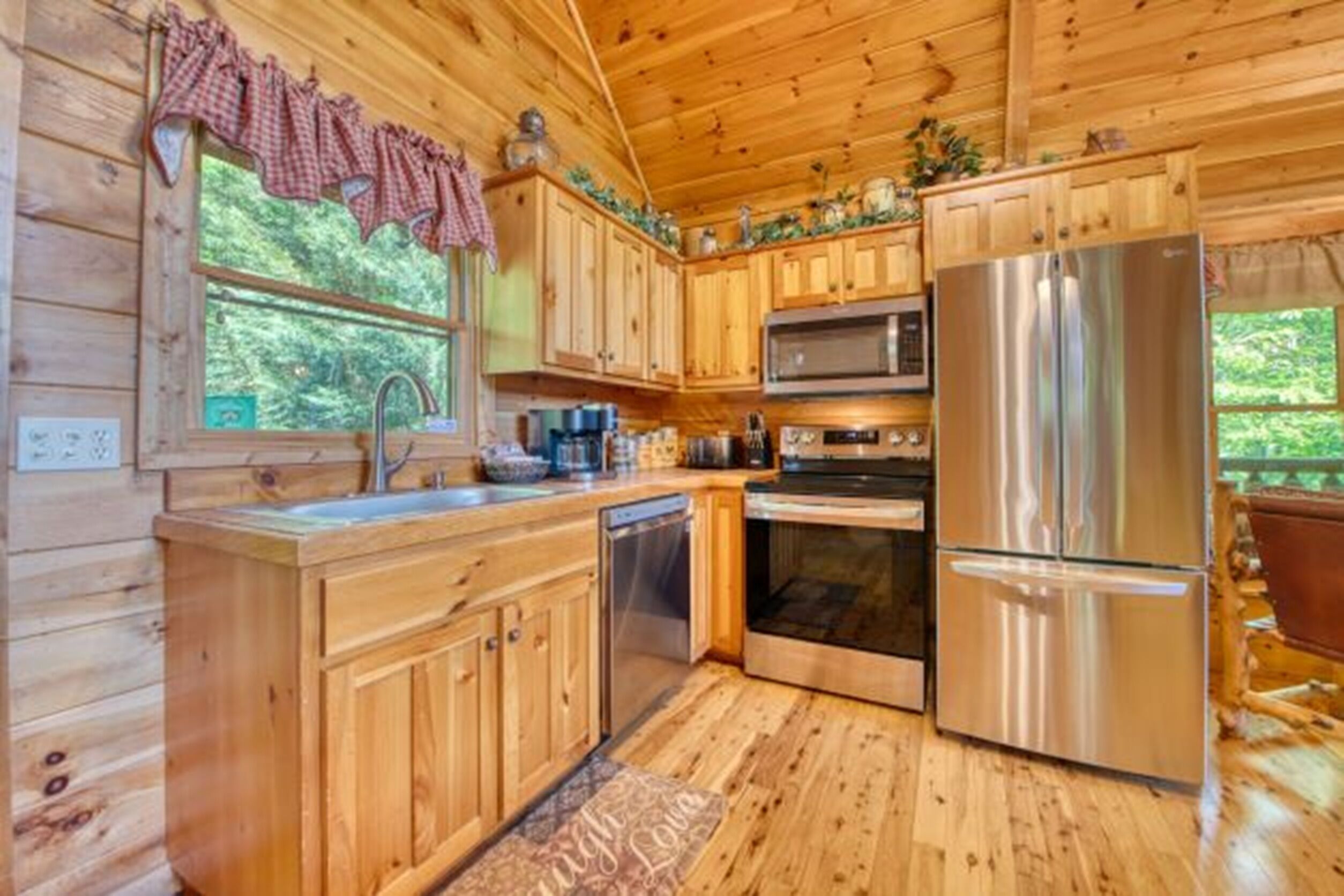 A wooden cabin kitchen with wooden cabinets, a stainless steel refrigerator, a microwave, and an oven.