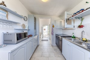 Una cocina con armarios blancos, microondas, fregadero y ventana.