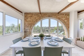 Ein Esstisch ist gedeckt mit Tellern, Gläsern und einer Mittelstück, mit einer Steinwand und einem Bogenfenster im Hintergrund.