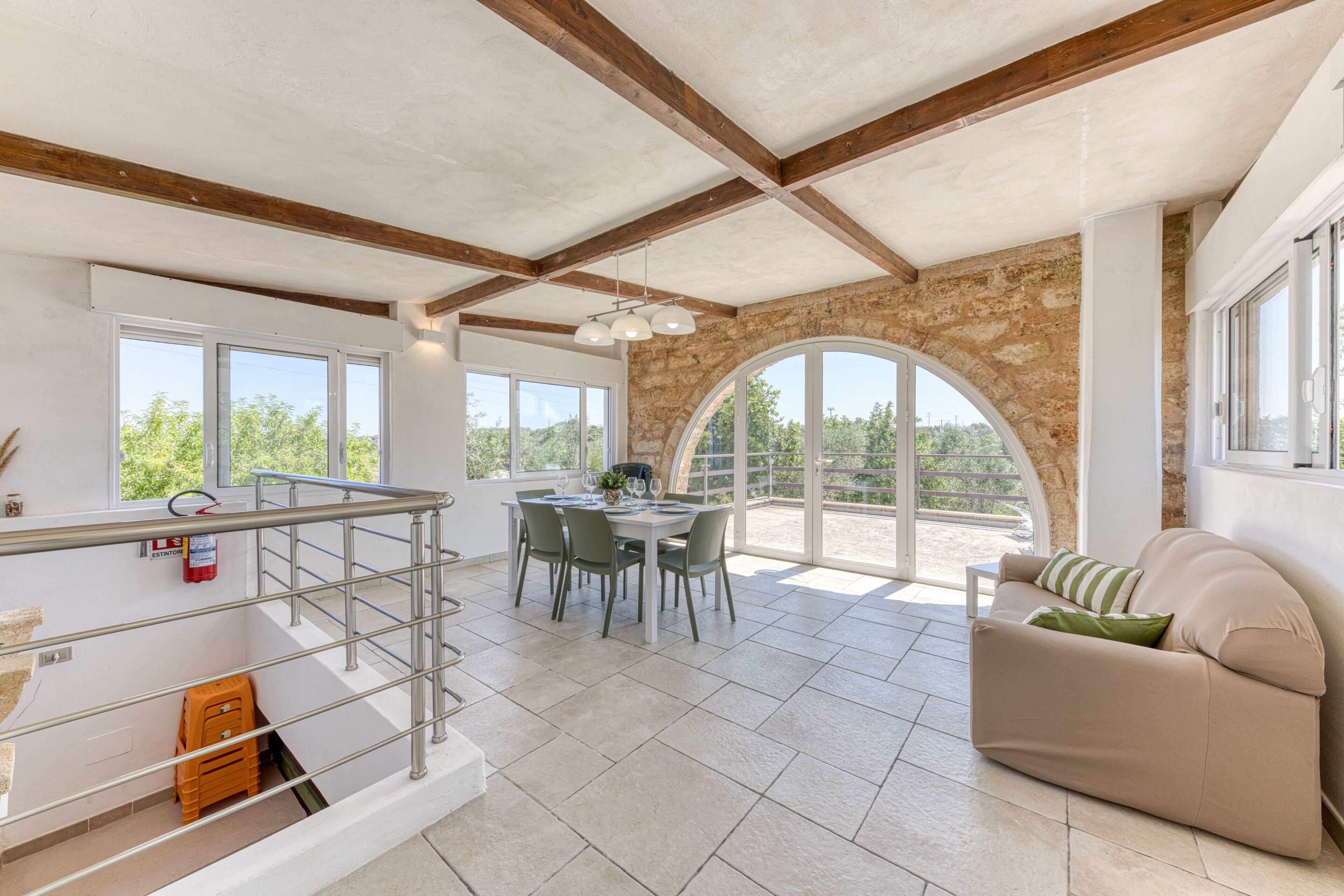 Una habitación amplia con comedor, un sofá y una escalera que conduce a un espacio exterior.