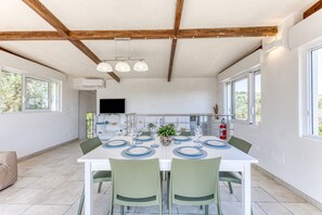 Un comedor con una mesa blanca preparada para cuatro personas, sillas verdes y una cocina al fondo.