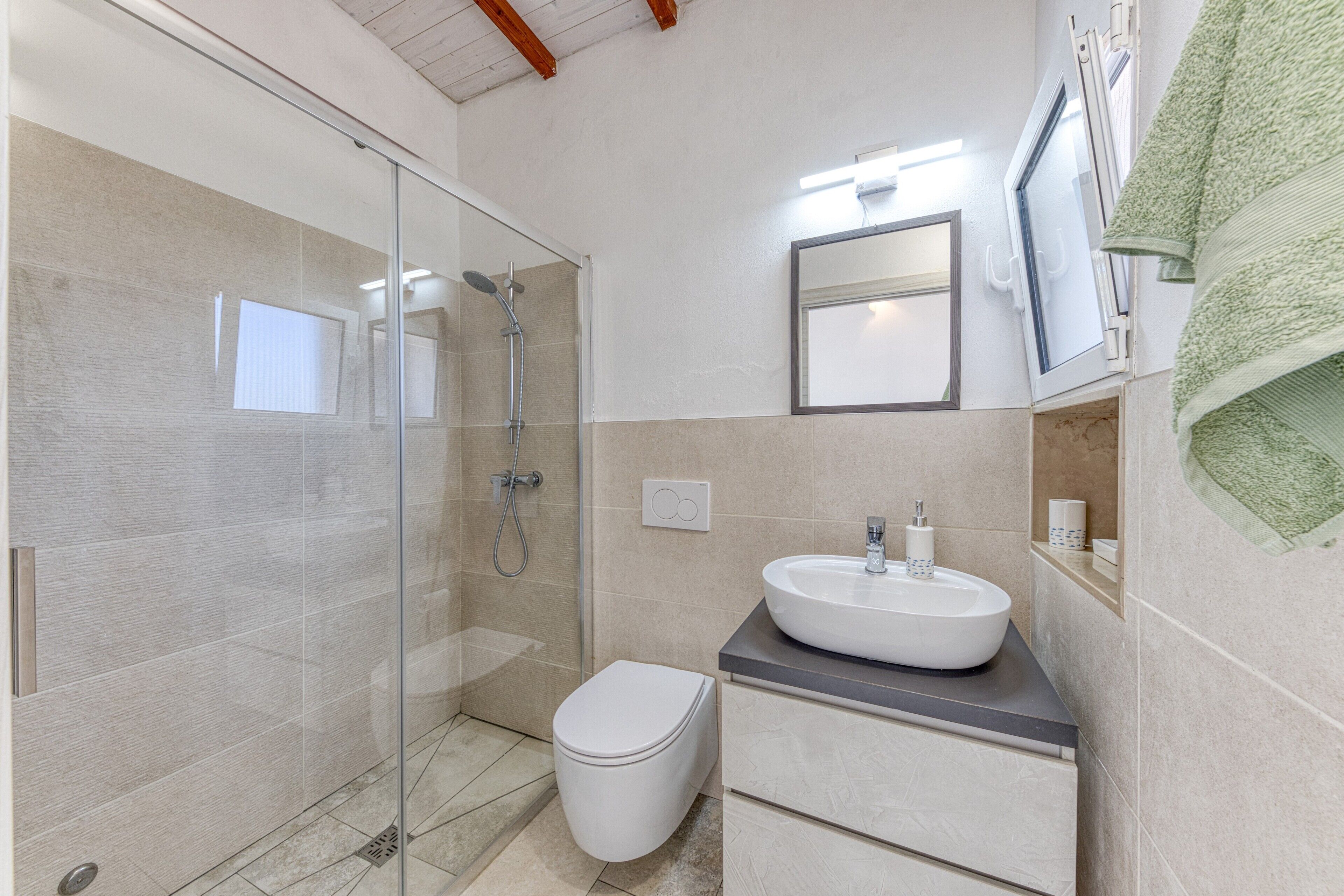 Un baño moderno con cabina de ducha de vidrio, inodoro blanco, lavamanos con espejo y una toalla colgada en la pared.