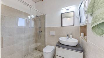 Un baño moderno con cabina de ducha de vidrio, inodoro blanco, lavamanos con espejo y una toalla colgada en la pared.