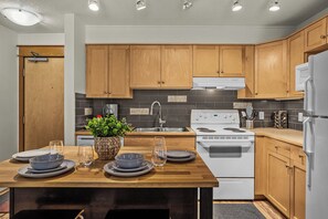 A modern kitchen with wooden cabinets, a stainless steel sink, and a white stove. - Quaint Canmore Basecamp | Views (Canmore)