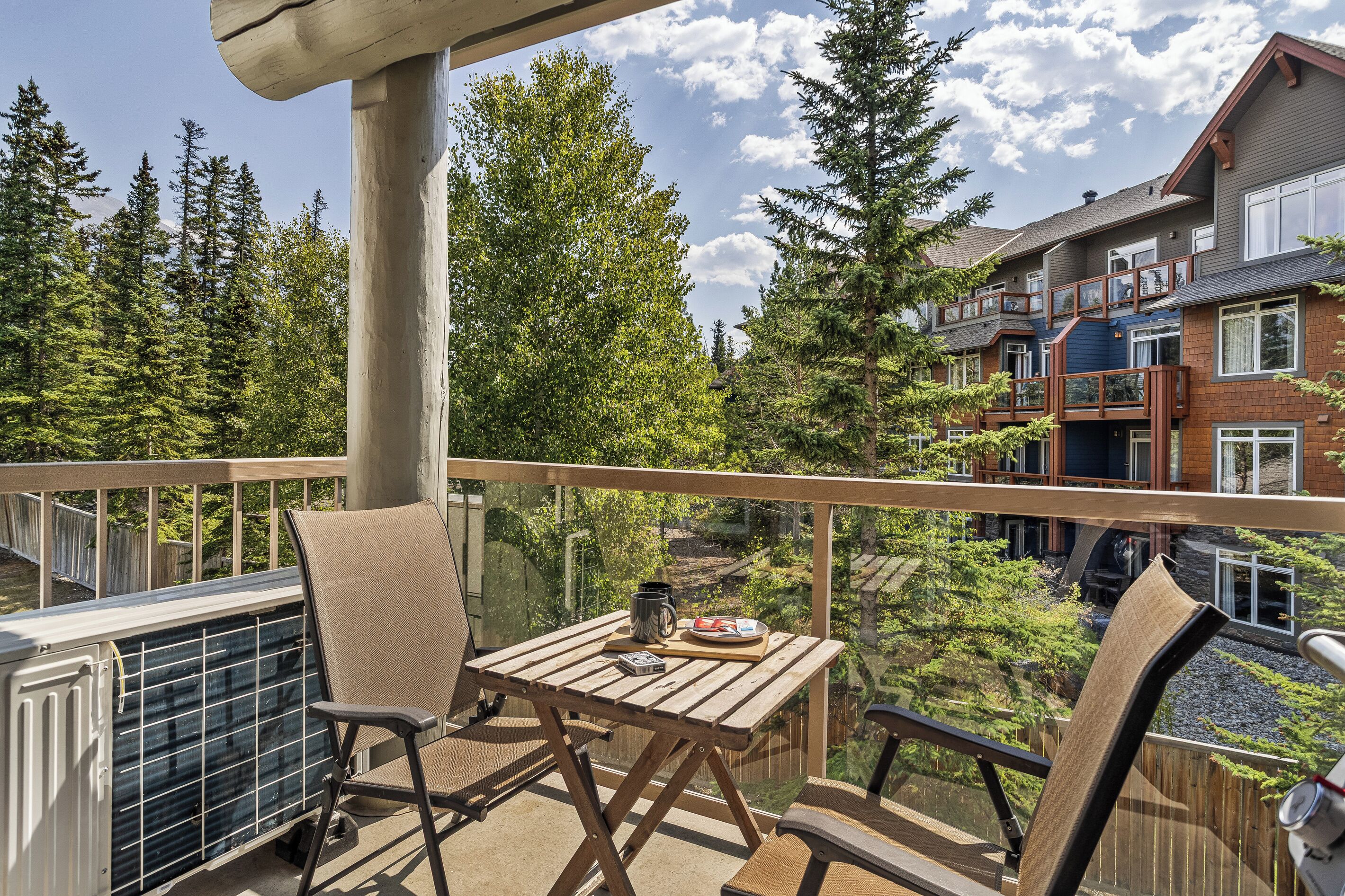 A balcony with a table, chairs, and a view of a forested area and buildings.