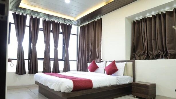 A bedroom with a large bed, curtains, a bedside table, and a nightstand. - Charming 9-bedroom hotel with AC in Indore
Fully Air Conditioned Budget Friendly (Indore)